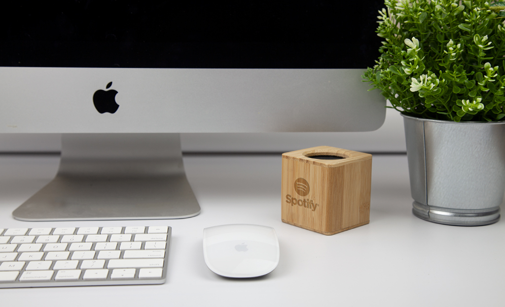 bamboo sustainable speaker engraved with a logo on a desk with a Mac and a plant
